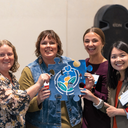 a group of smiling women hold a large puzzle piece