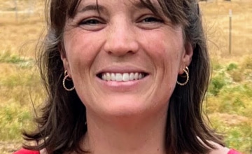a smiling woman with shoulder-length brown hair wearing a red sleeveless top