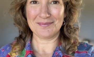 a smiling woman with light brown hair wearing a multi-colored button up shirt