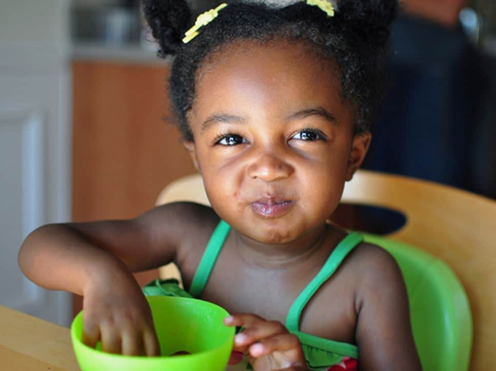 a smiling female toddler eats a snack
