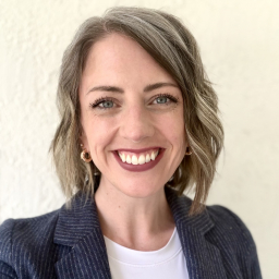a smiling woman with shoulder-length sandy blonde hair wearing a white shirt with navy blazer