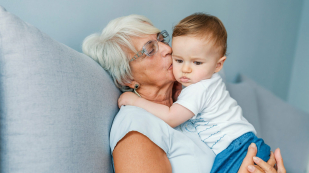 A grandmother holds and kisses her grandchild.