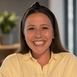 a smiling woman with long brown hair wearing a black headband and yellow button up dress shirt