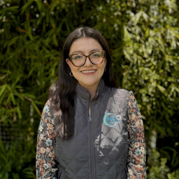 a smiling woman with long dark hair wearing glasses, a sleeveless puffer jacket, and floral shirt